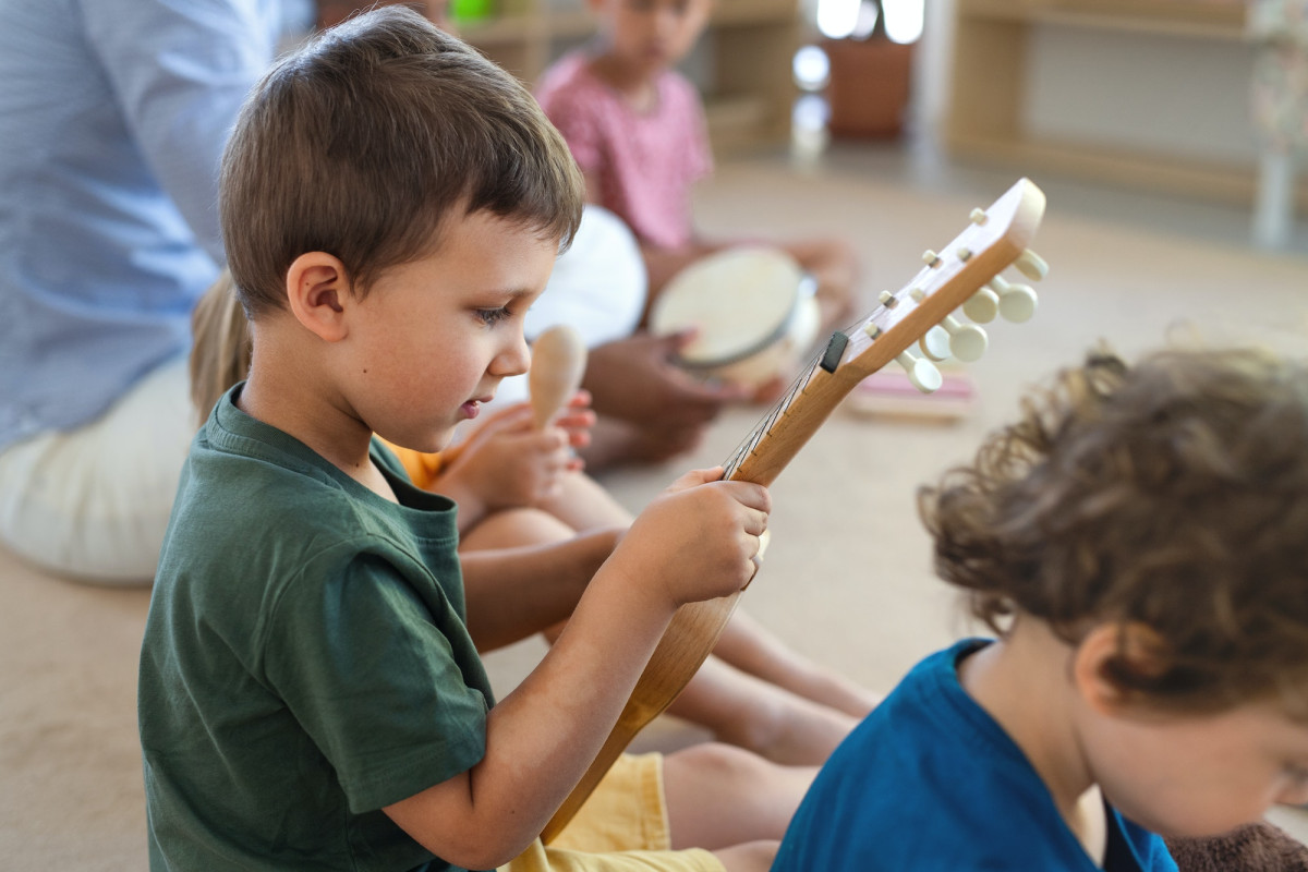 Nursery school children sitting on floor indoors in classroom, playing musical instruments.